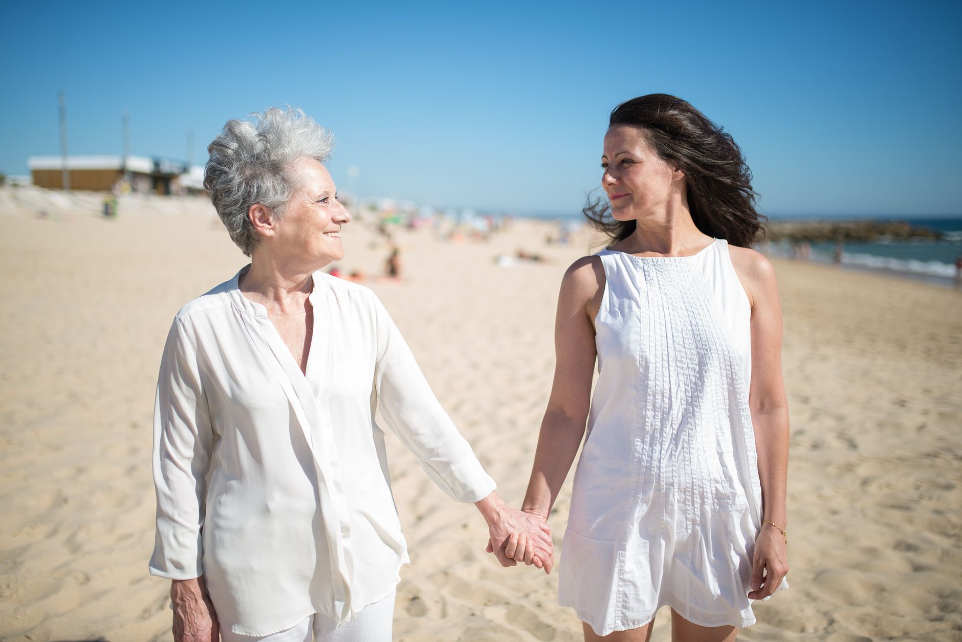 An adult daughter and her elderly mother holding hands on the beach