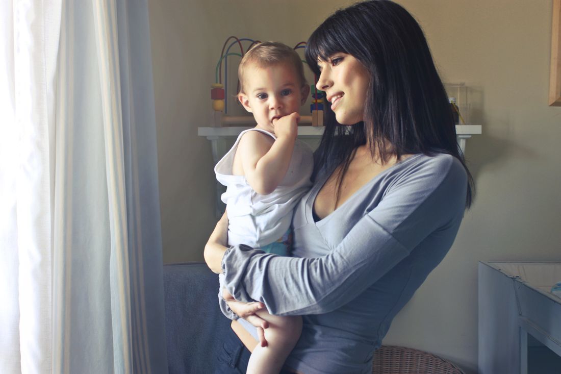A mother holding her toddler by a sunlit window