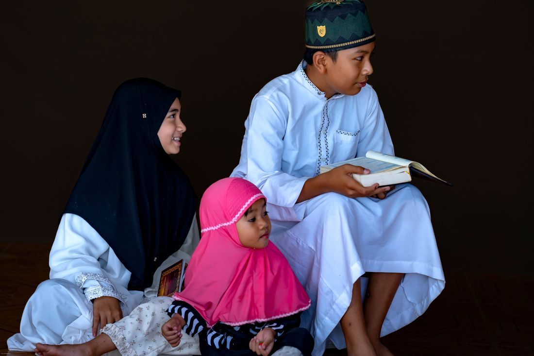 Muslim children together, a boy reading as the younger ones look on