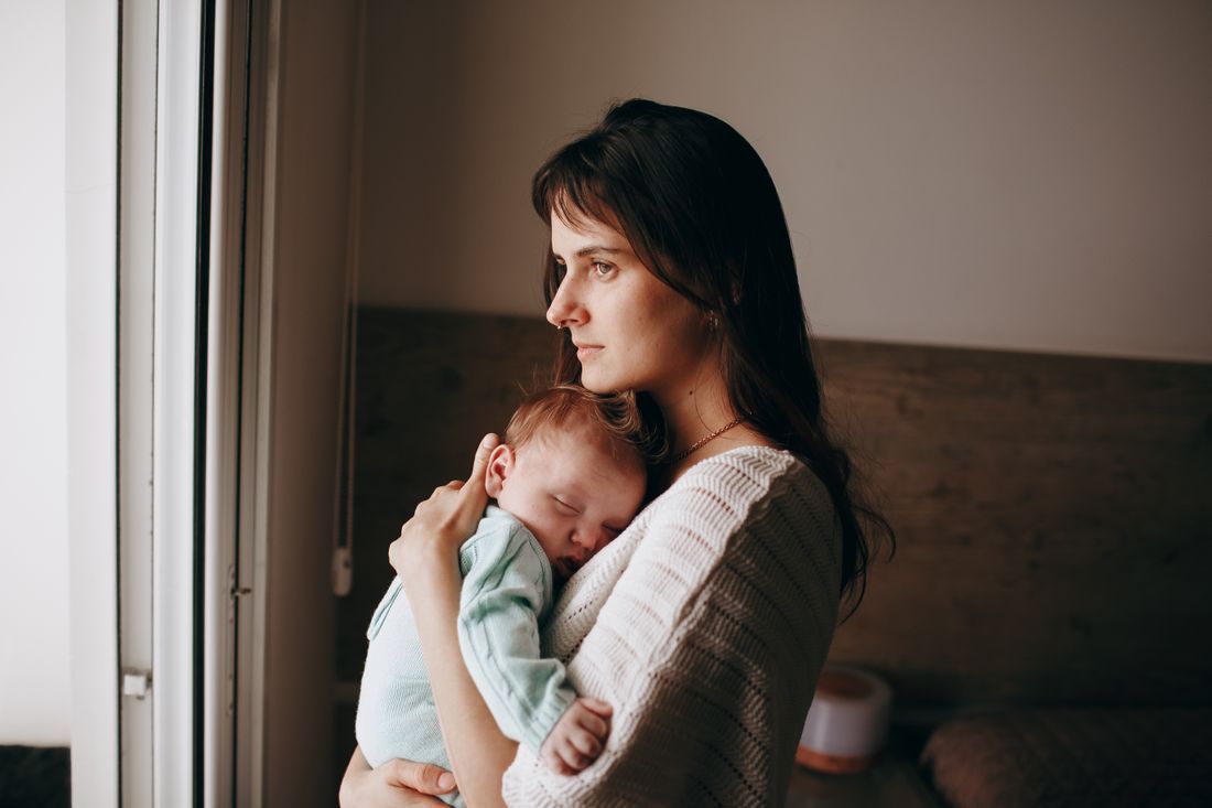 A weary mother holding her sleeping newborn by a window
