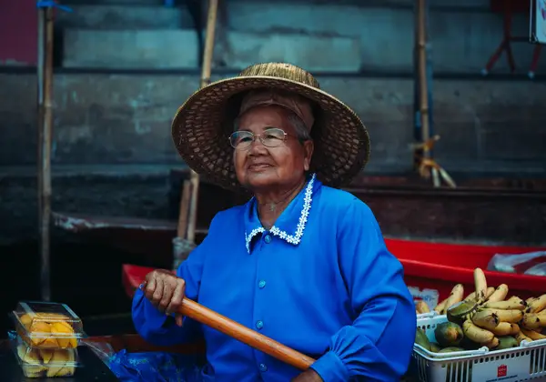 An elderly Thai woman selling fruit at a floating market