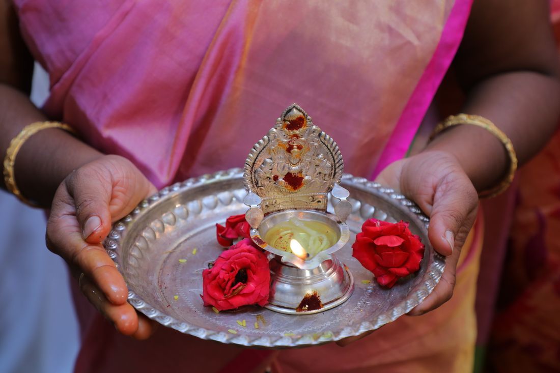 A woman in a sari holding an aarti plate with a flame and flowers