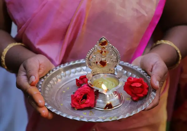 A woman in a sari holding an aarti plate with a flame and flowers
