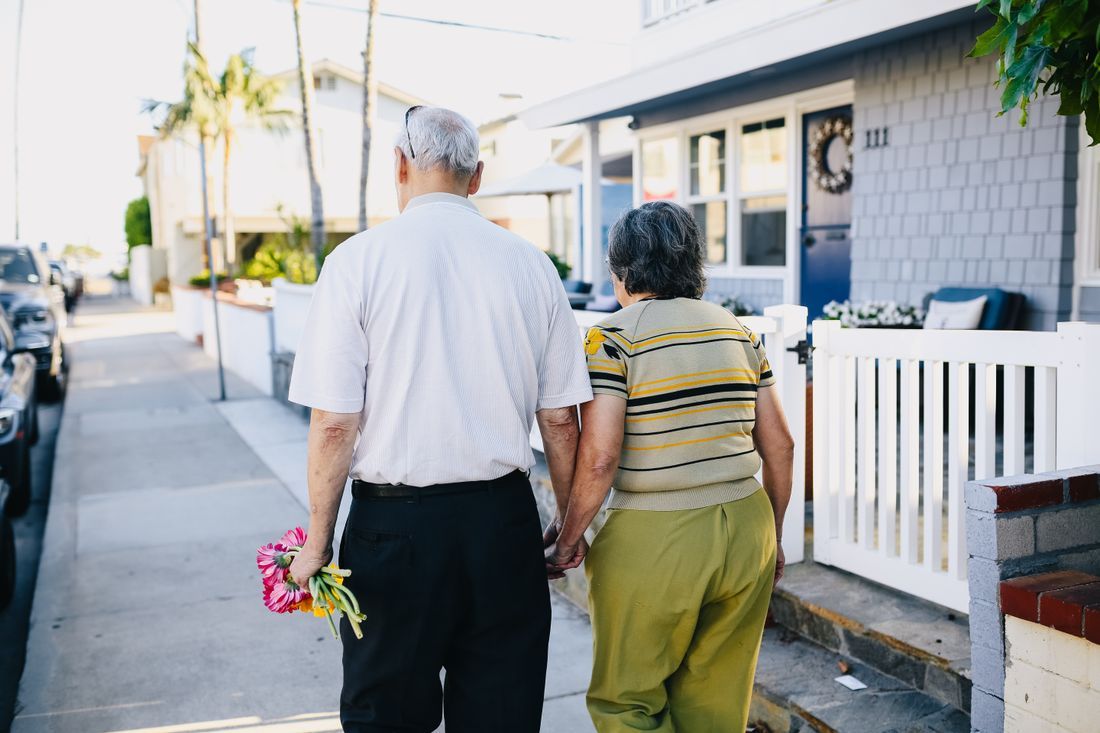 An older husband and wife walking together, he carrying flowers