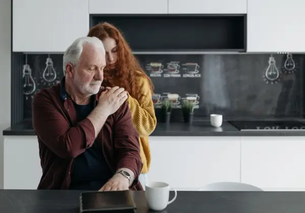 A daughter embracing her aging father from behind in the kitchen