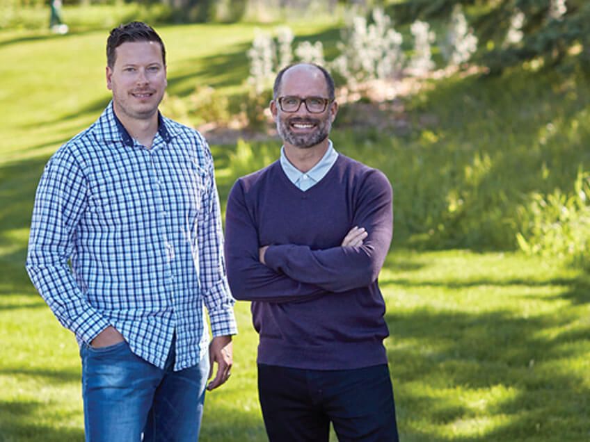 Neil Mackimmie and Brett O'Reilly standing together in a grassy field, surrounded by greenery and open space. 