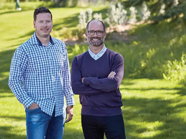 Neil Mackimmie and Brett O'Reilly standing together in a grassy field, surrounded by greenery and open space. 