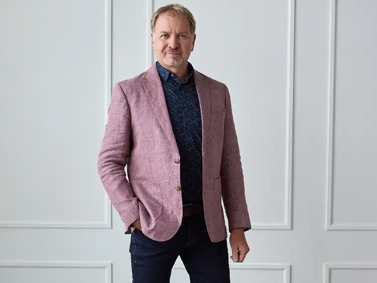 Richard Bukarewicz wearing a mauve blazer and standing against a white wall.