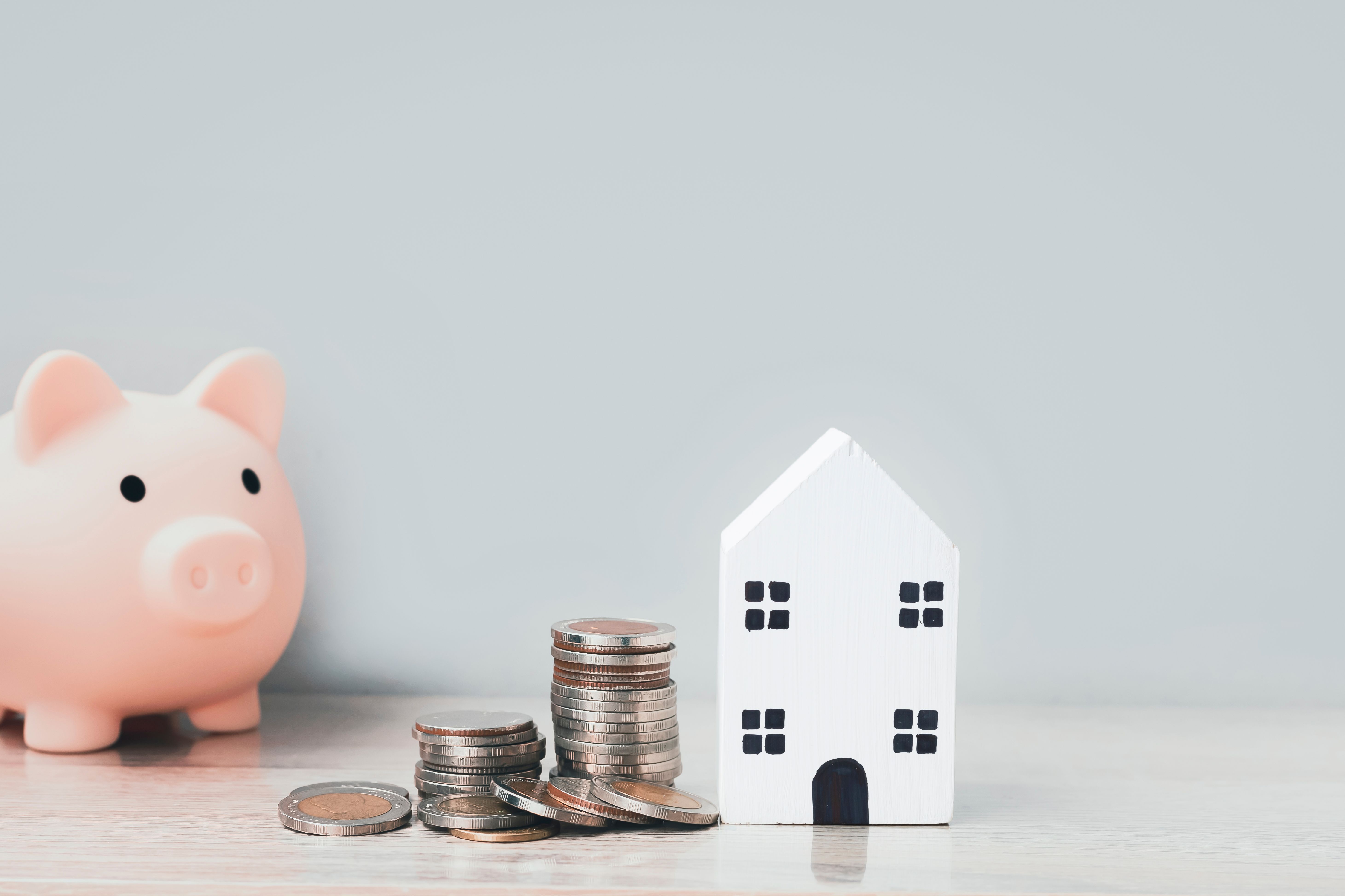 Piggy bank, coins and a model house representing savings for homeownership.