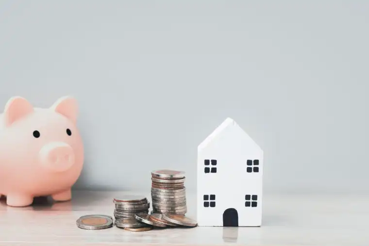 Piggy bank, coins and a model house representing savings for homeownership.