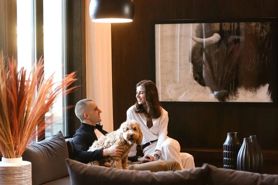 A man and woman relax on a couch with a dog sitting comfortably between them.  