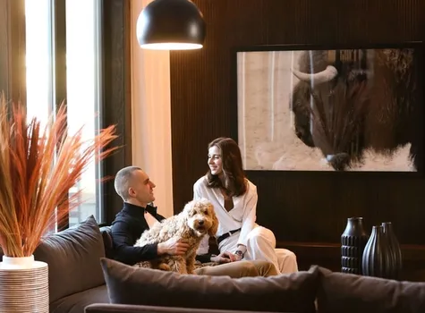 A man and woman relax on a couch with a dog sitting comfortably between them.  