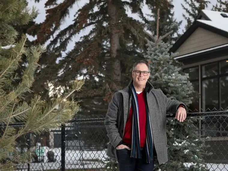 A man poses by a fence, with a tree and house behind him
