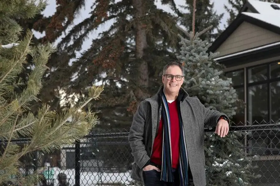 A man poses by a fence, with a tree and house behind him