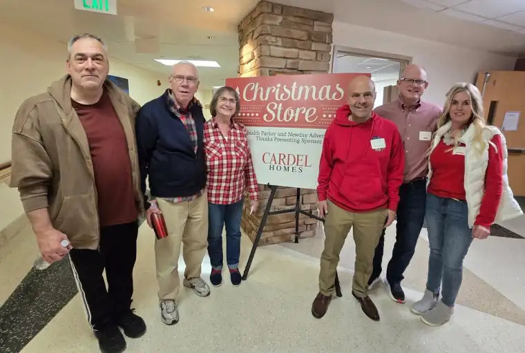 Cardel Homes team members and volunteers standing beside the AdventHealth Parker Christmas Store sign at the hospital.