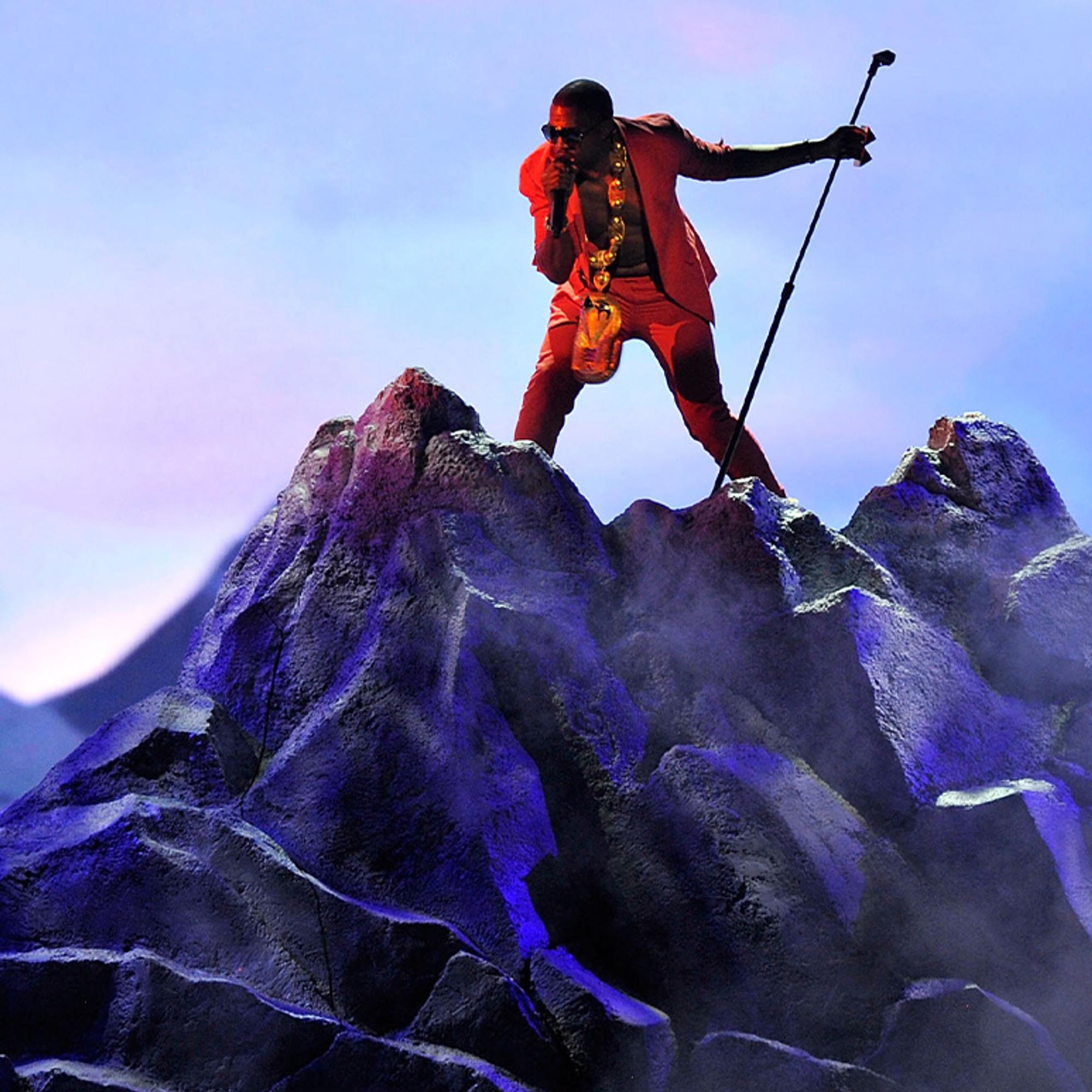 Kanye West in red performing on a rocky blue stage set