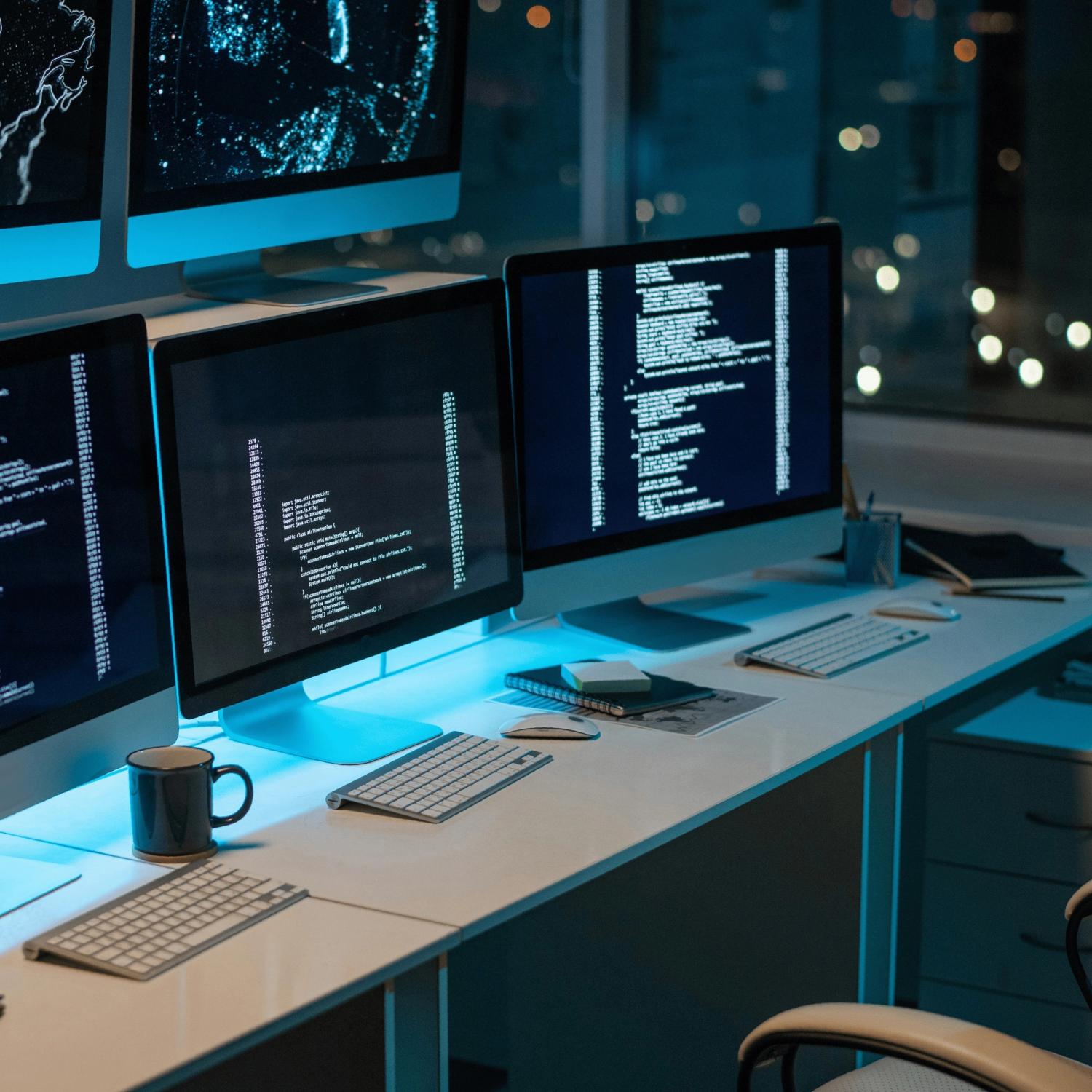 Desk with three computer monitors displaying data.