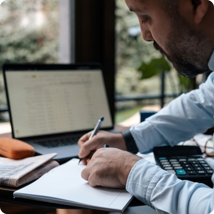 Male security expert writing on notepad at table with laptop.