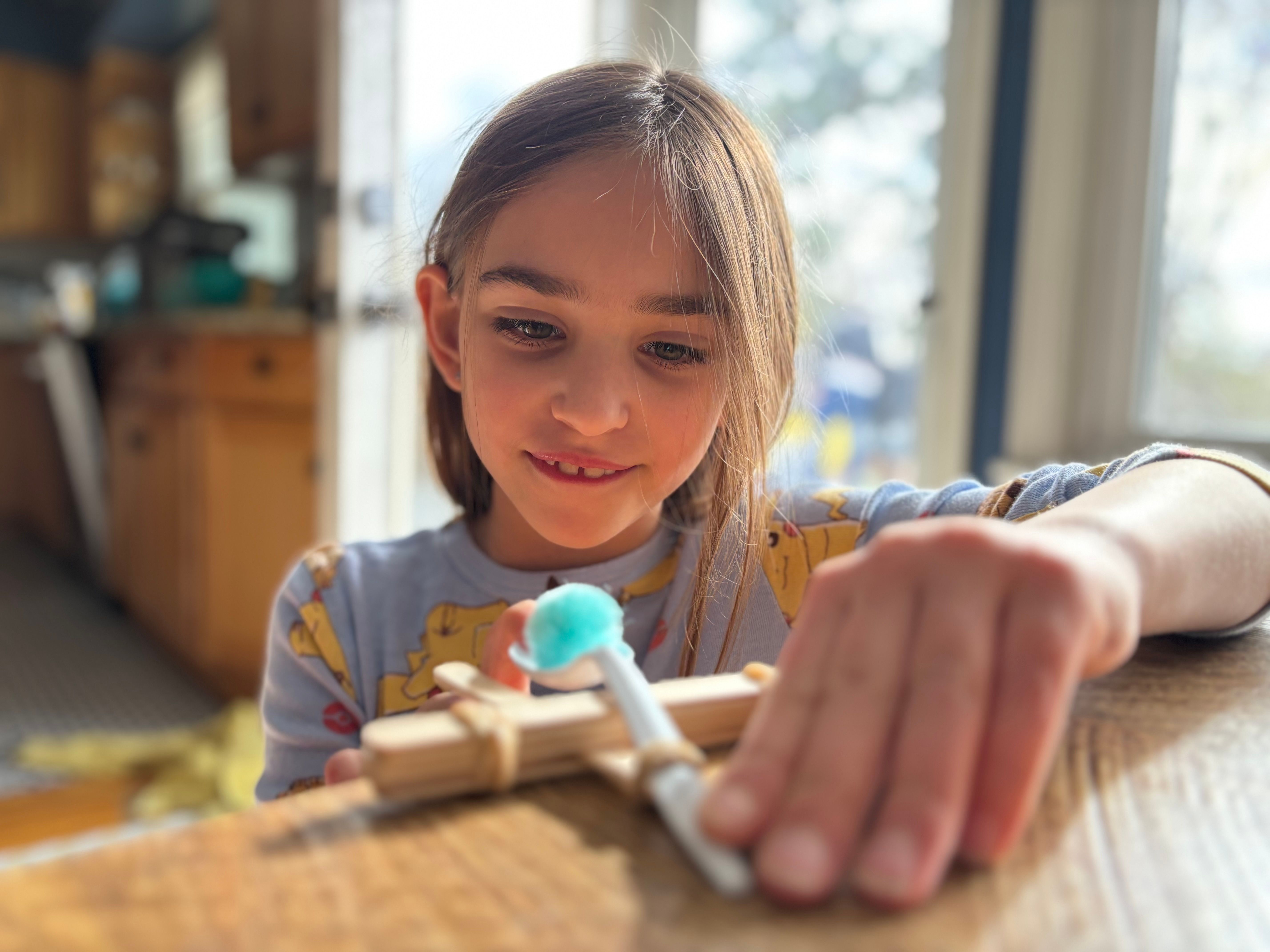 A girl plays with a popsicle stick and spoon catapult she made with GlueStick