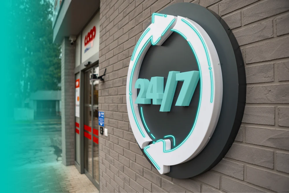 A 24/7 sign on the brick wall beside the entrance of a COOP Jednota store
