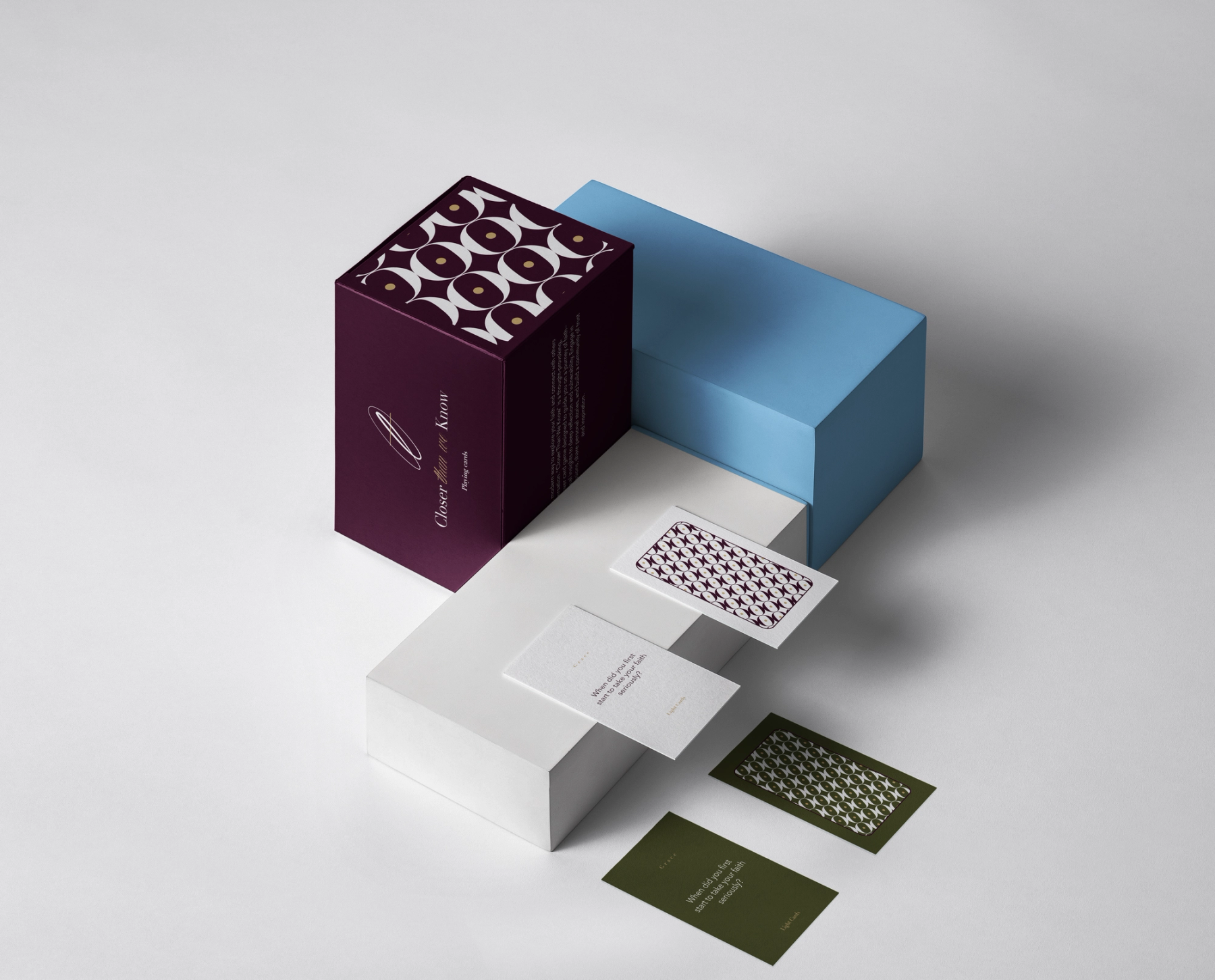 A stylized presentation of the "Closer than we know" card game. The deep plum box features a signature geometric pattern in white and gold. Displayed on modern blue and white structural blocks, the layout highlights the physical card components, contrasting the minimalist text prompts against the bold patterned backs.