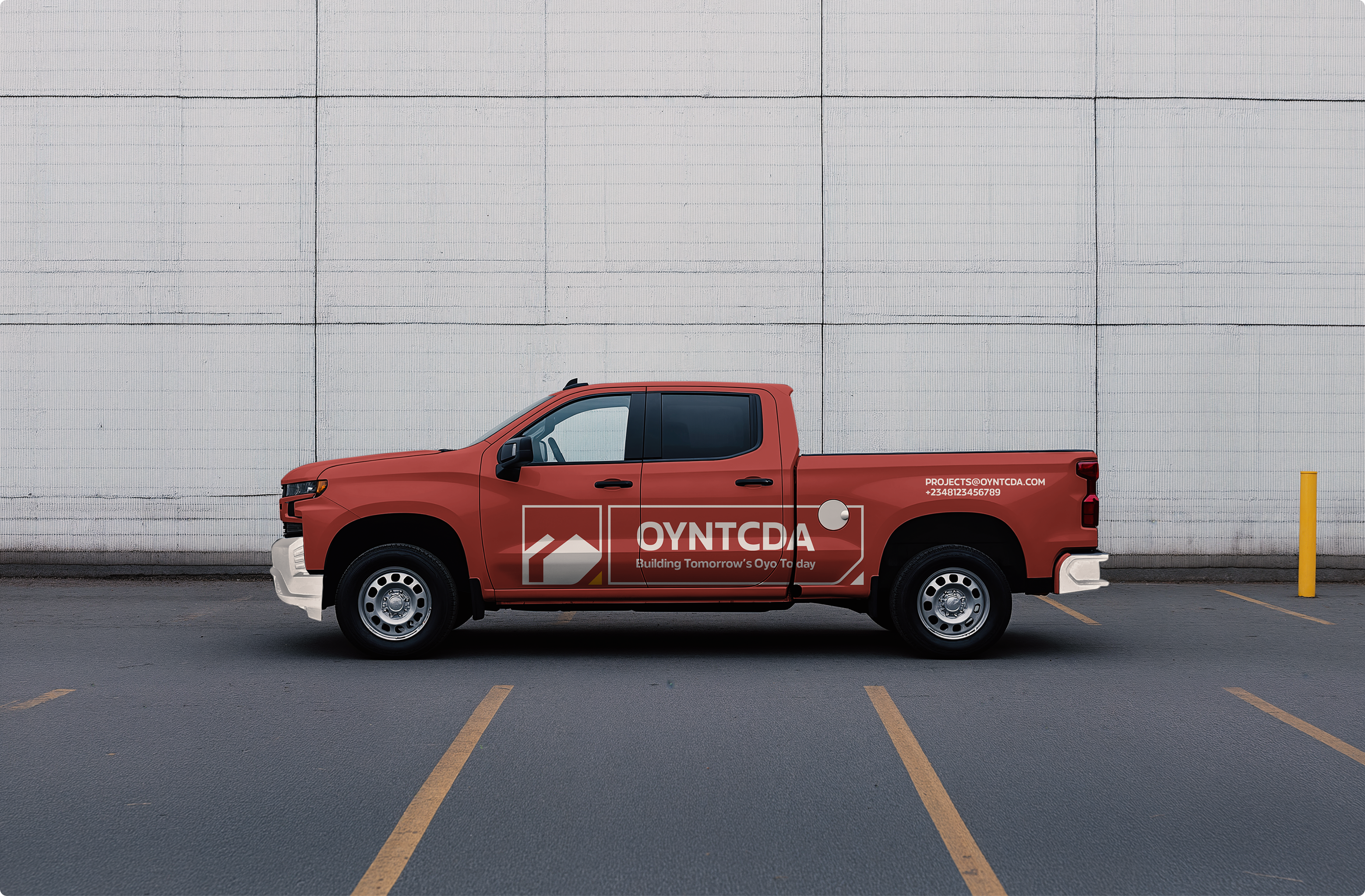Red OYNTCDA pickup truck with a white identity lockup against a concrete wall