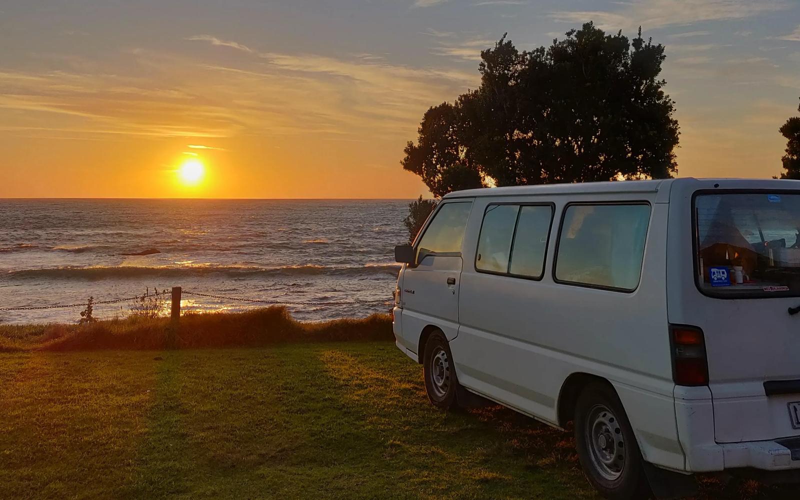 Camper bij zee tijdens zonsondergang