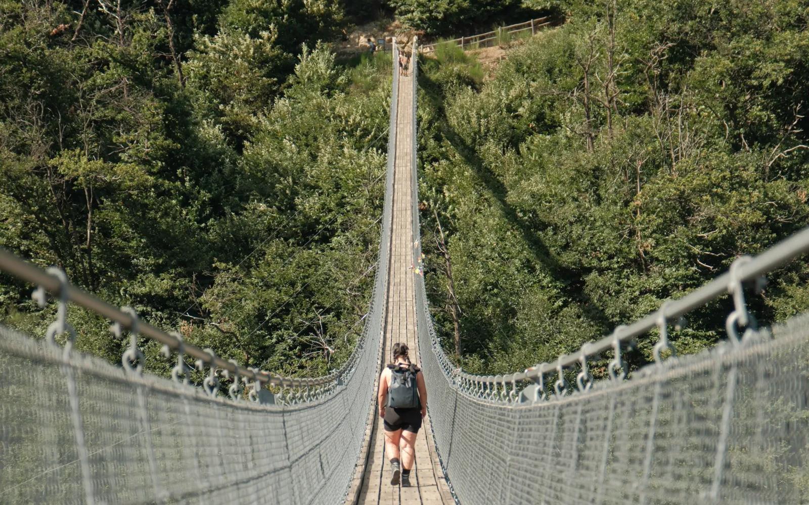 Persoon op een hoge hangbrug boven een groen ravijn