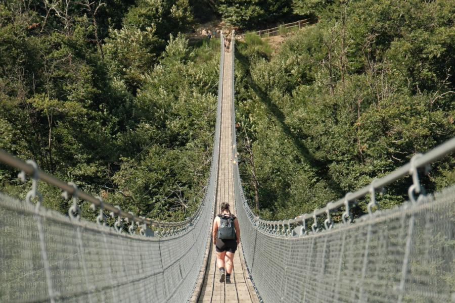Persoon op een hoge hangbrug boven een groen ravijn