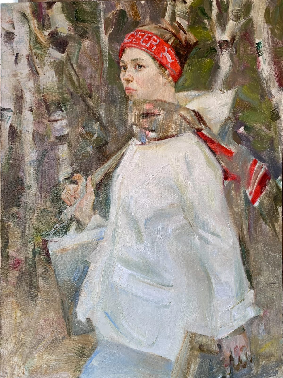 Young woman in a white dress and red headscarf seated among birch trees.