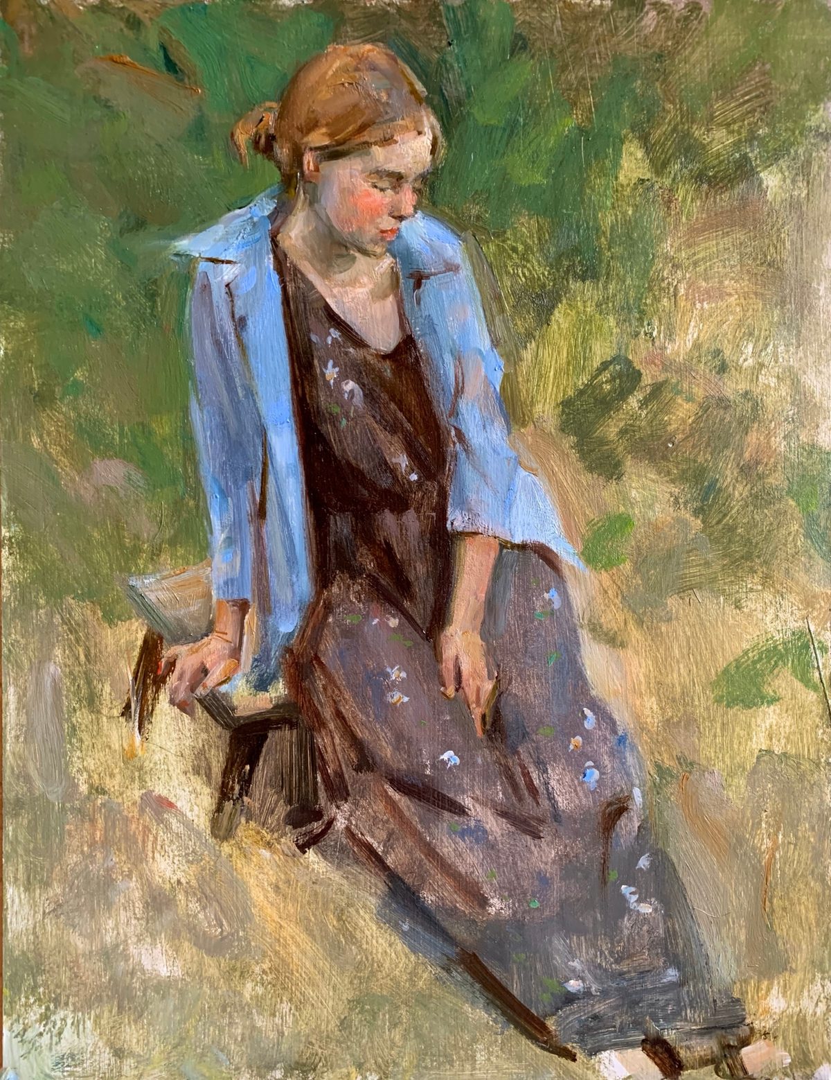Young woman in a blue jacket and dark floral dress seated in grass.