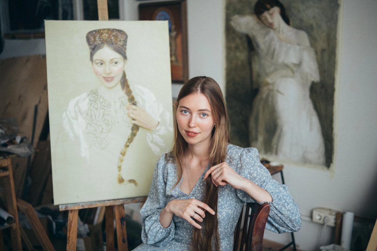 Anna Kondrateva seated in her studio beside two paintings.