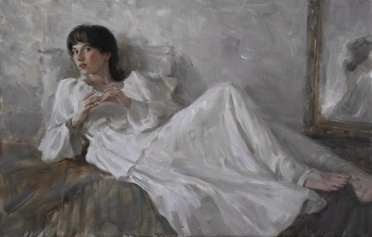A woman in a white dress reclining beside a large framed mirror in a muted grey interior.