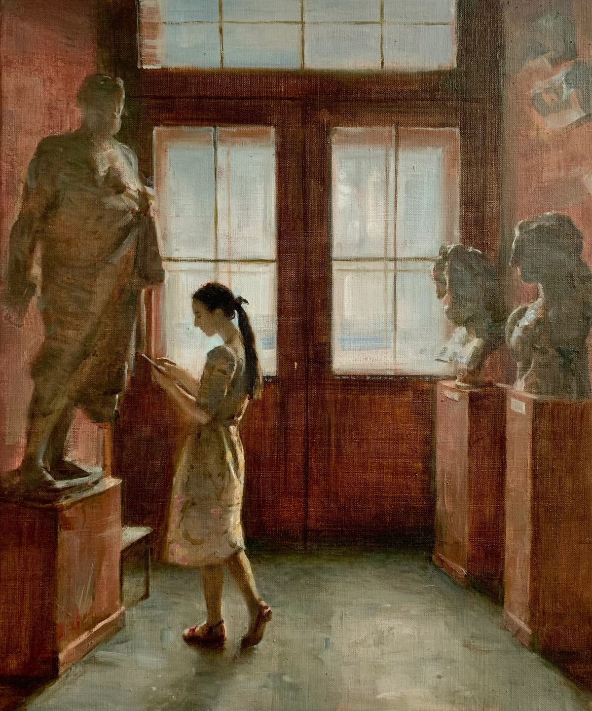 Woman holding a sketchbook in a gallery with plaster sculptures and tall windows.