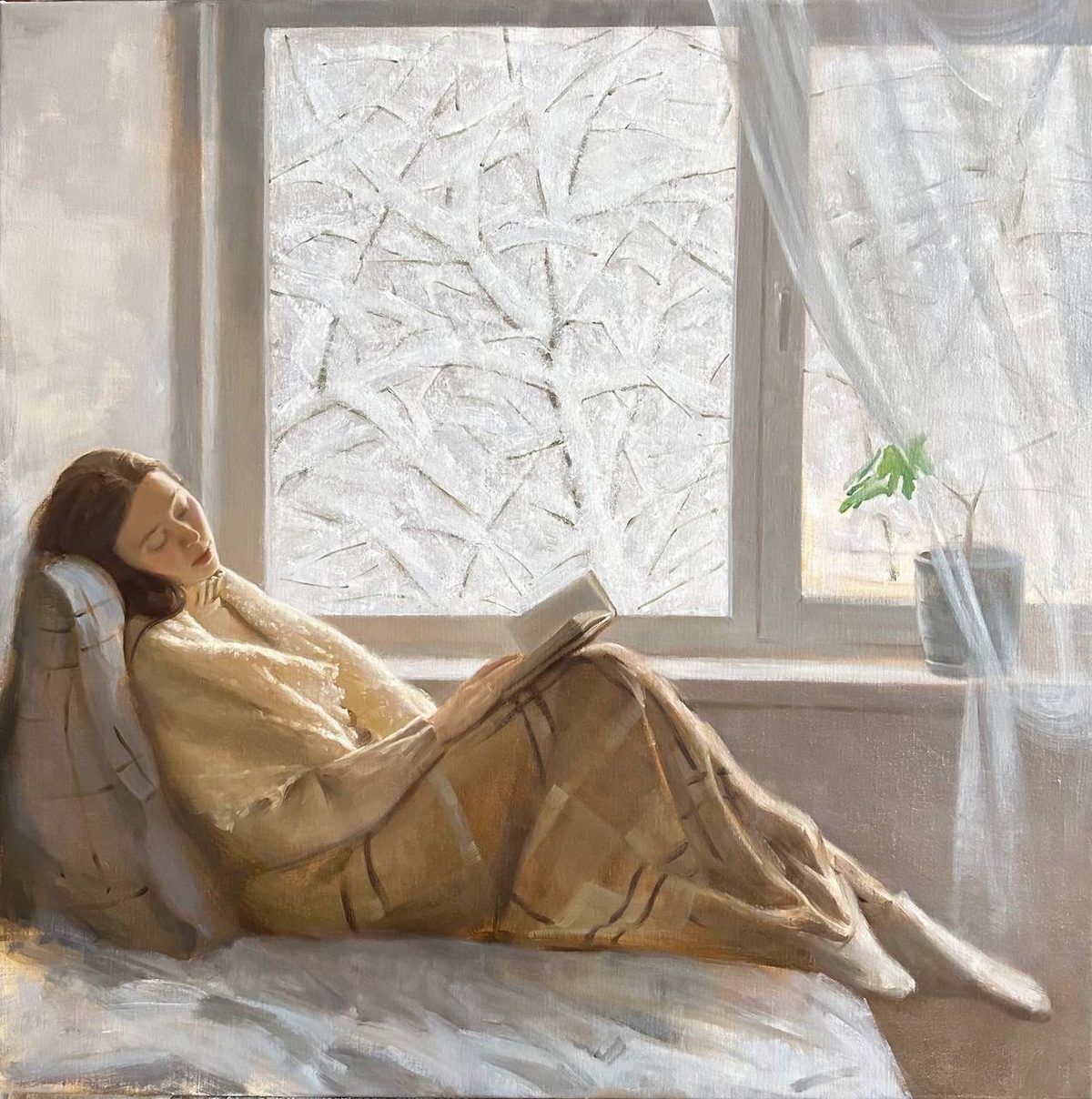 Woman reclining with an open book before frost-covered windows.