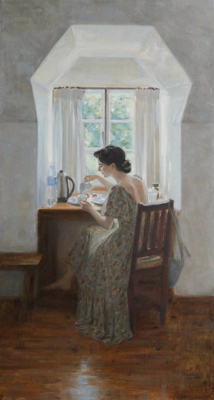 Woman seated at a table by a bright bay window.