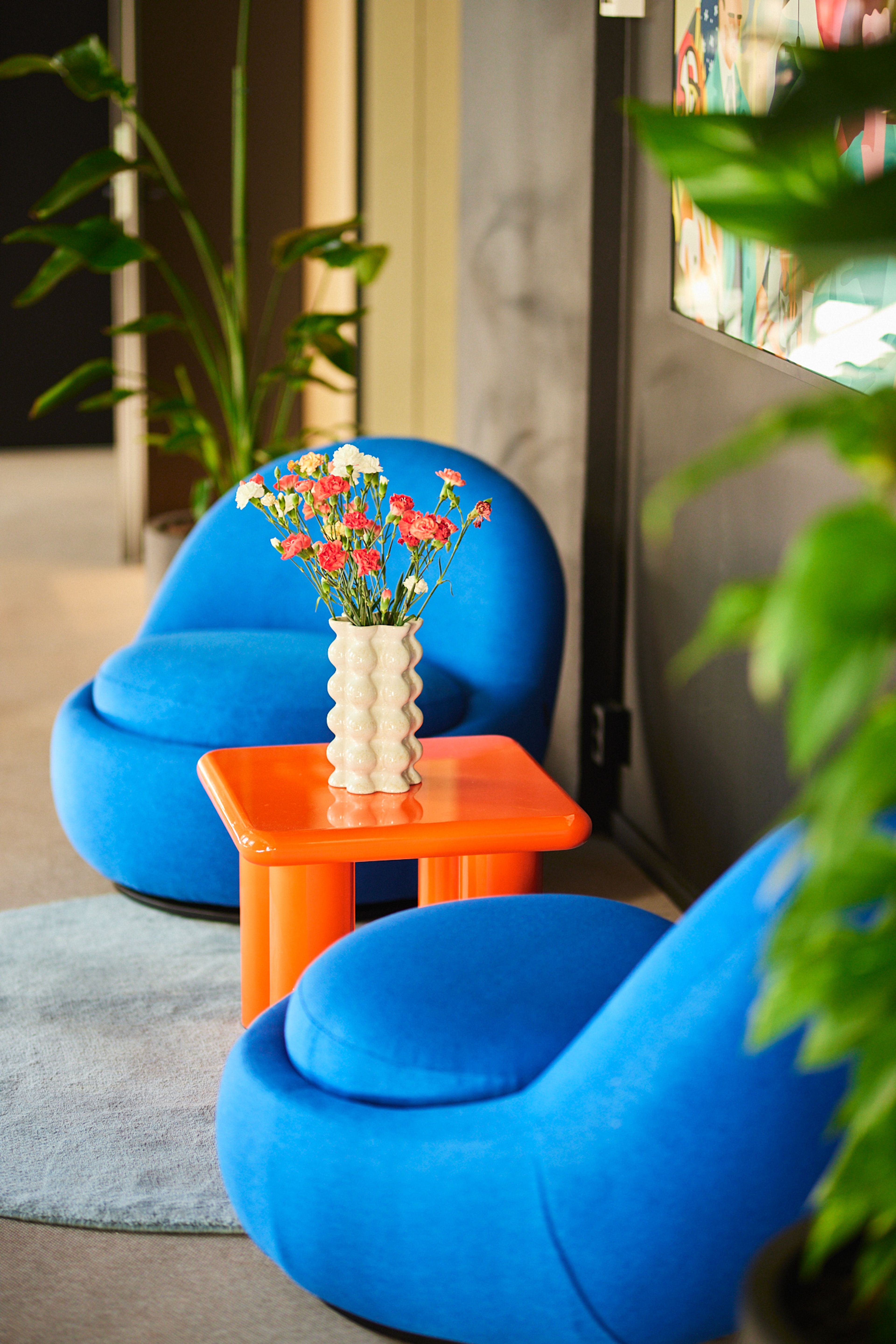 two blue chairs and an orange table with a vase of flowers on it .