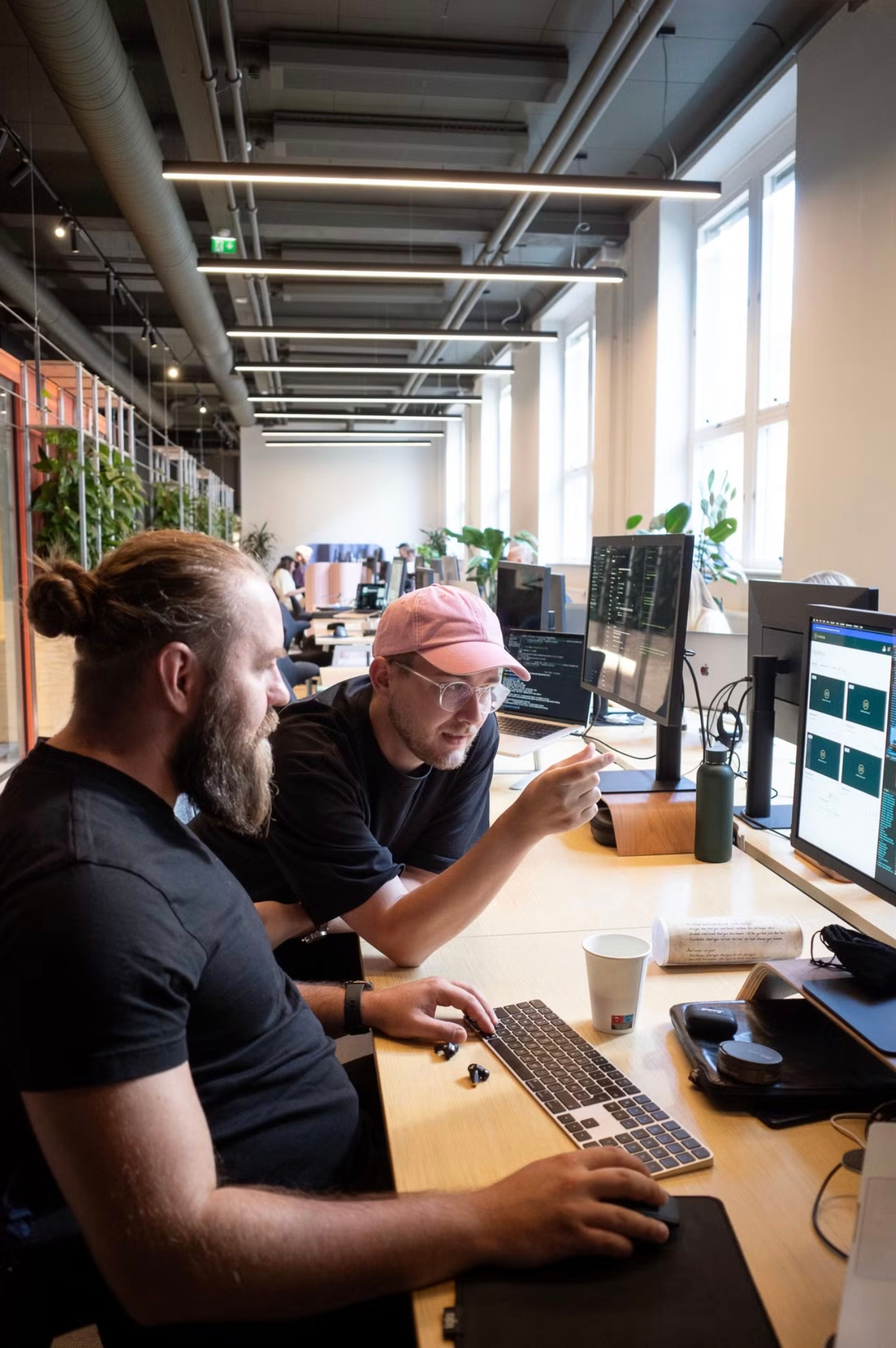 two men are sitting at a desk looking at a computer screen