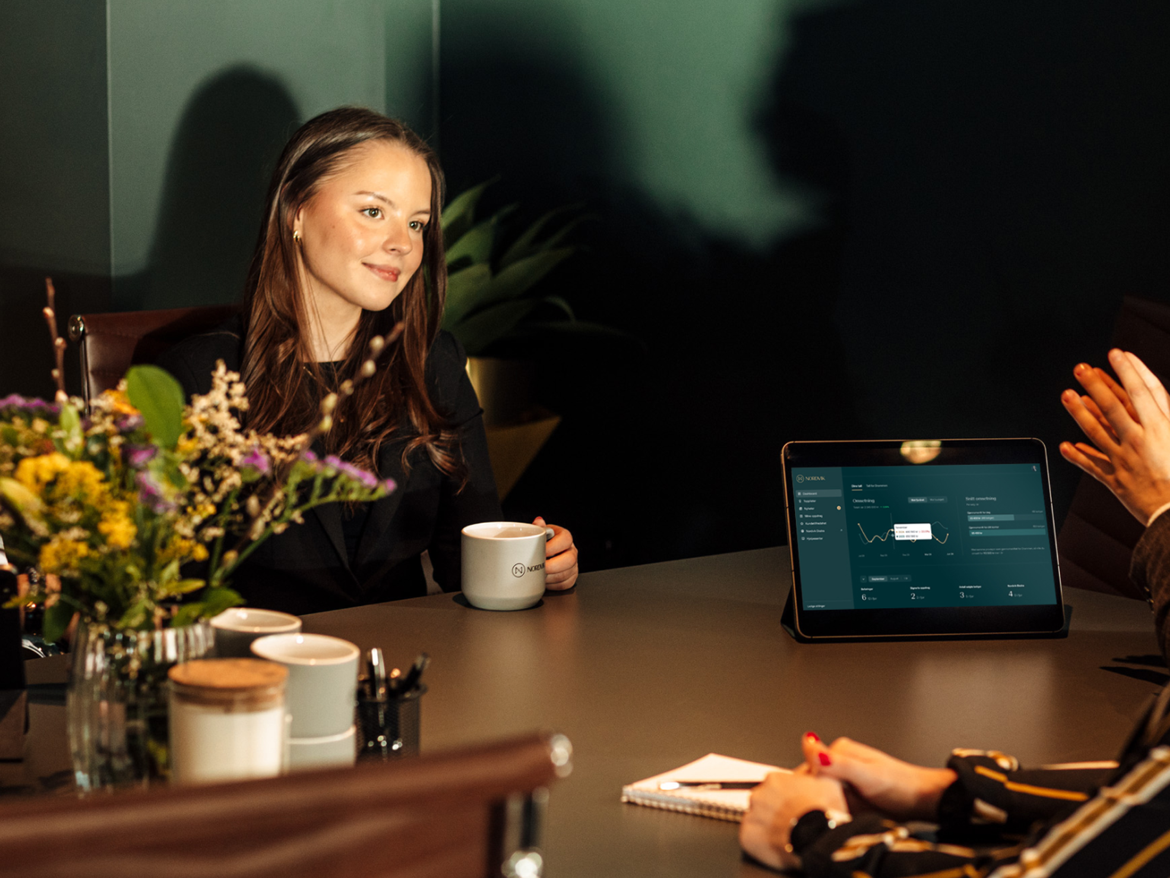 a woman sits at a table with a cup of coffee and a tablet with a graph on it