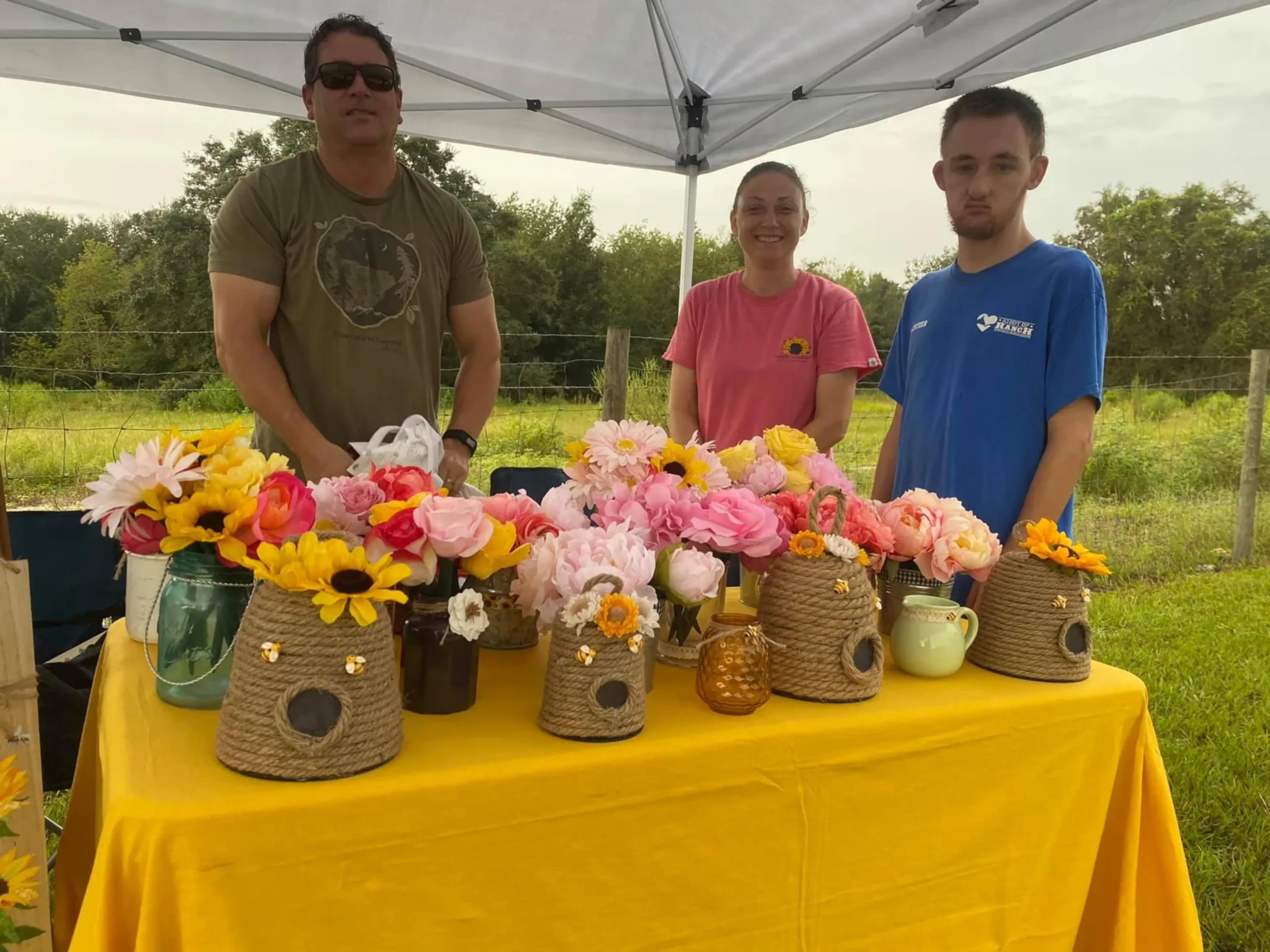 Three vendors behind a yellow table of flowers in vases at Market Day