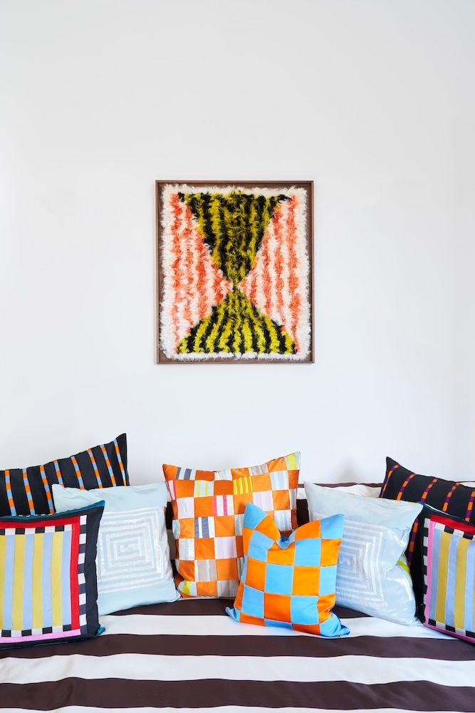 A framed, textured abstract artwork hangs above a bed adorned with colorful, patterned throw pillows and striped bedding.