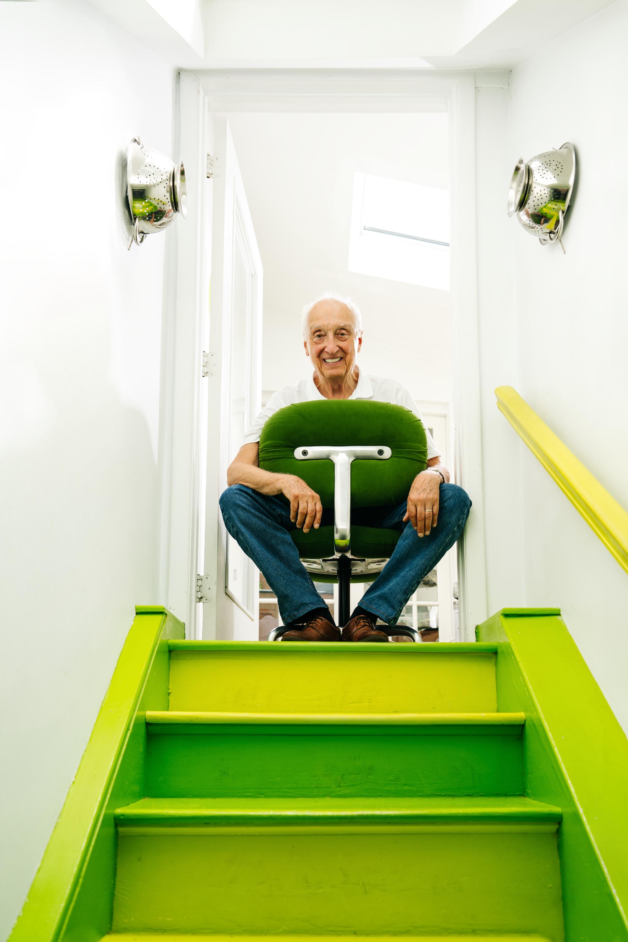 Bruce Hannah sat on a Knoll Morrison Hannah Chair at top of lime green staircase