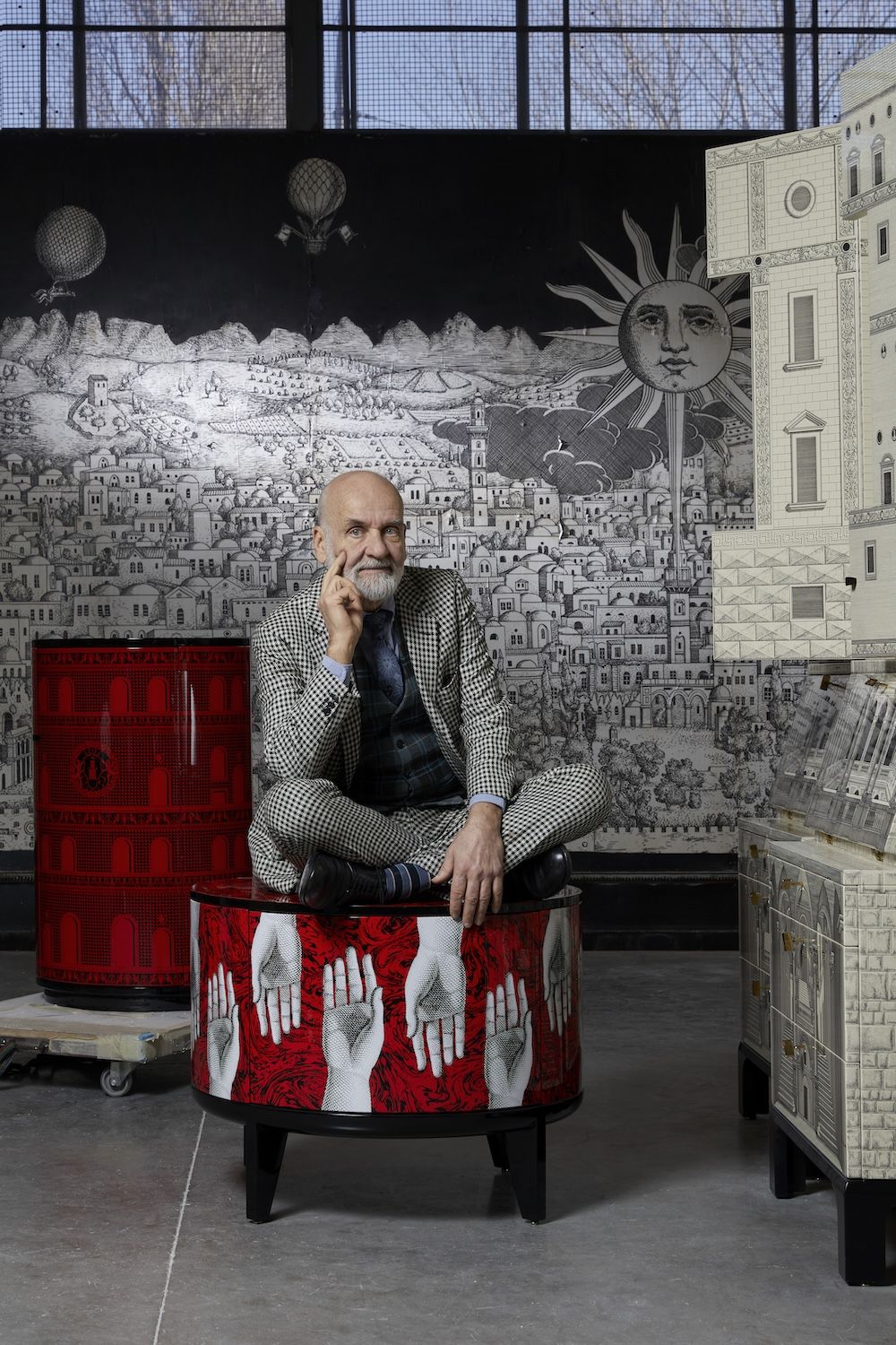 Barnaba Fornasetti seated on a small red cabinet decorated with a repeated hand motif