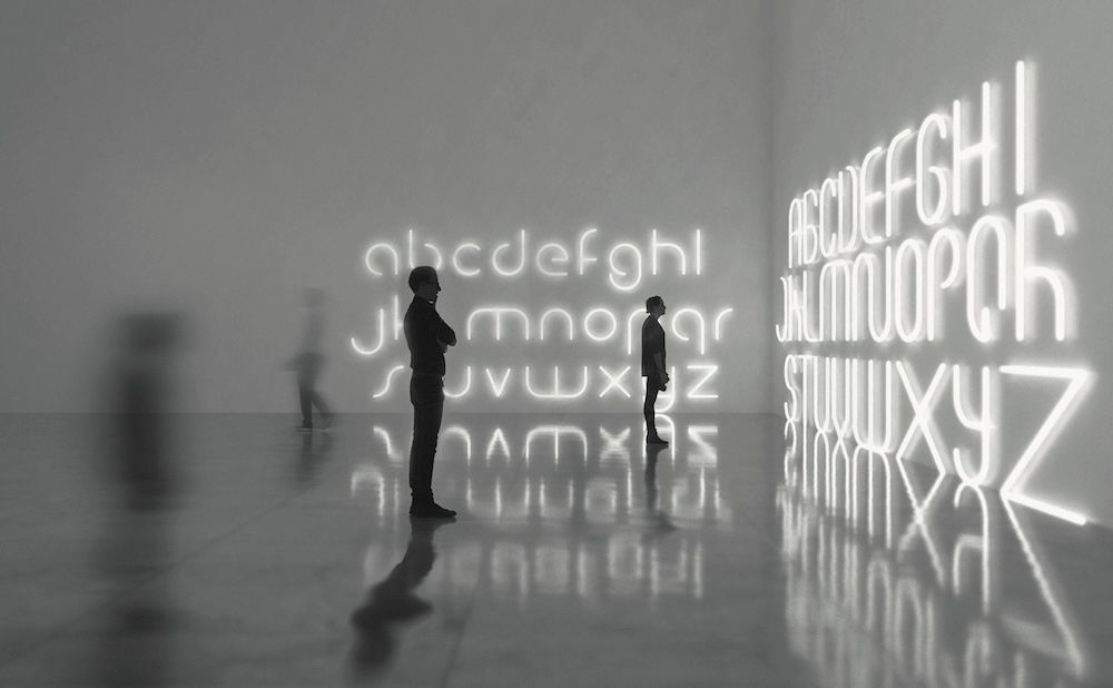 Silhouettes of people observing illuminated alphabet letters on a wall