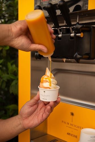 Someone serving soft serve ice cream with a yellow sauce on top