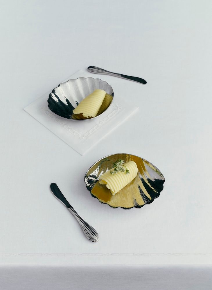 Two silver butter dishes with butter knives and butter scoops in them 