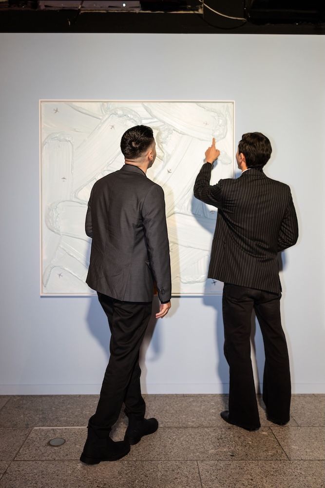 Two men looking at an artwork in suits and pointing to the white painting 