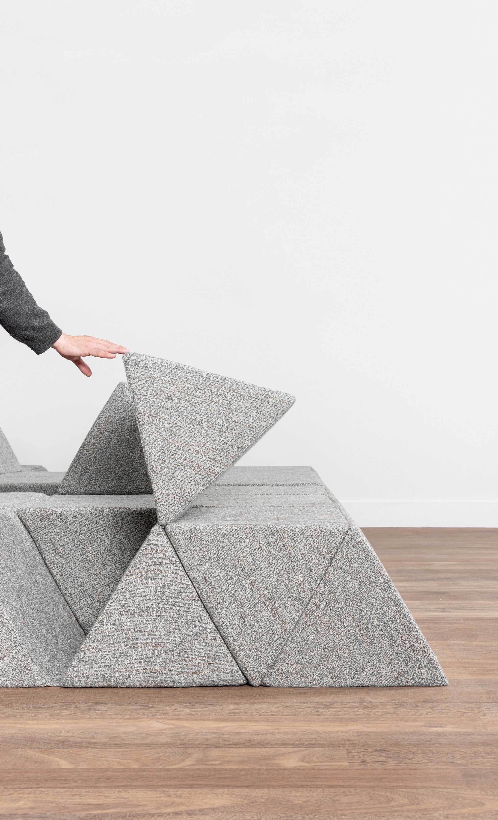 Hand touching grey modular seating arranged in peak-like forms