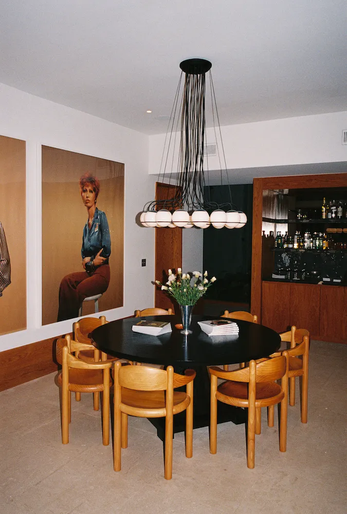 A dining table with hanging light above and portraits on the left hand wall