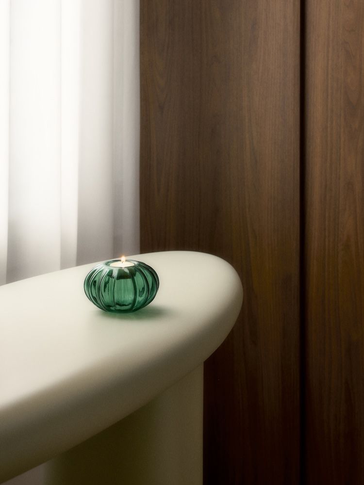A green candle holder on white table with candle lit